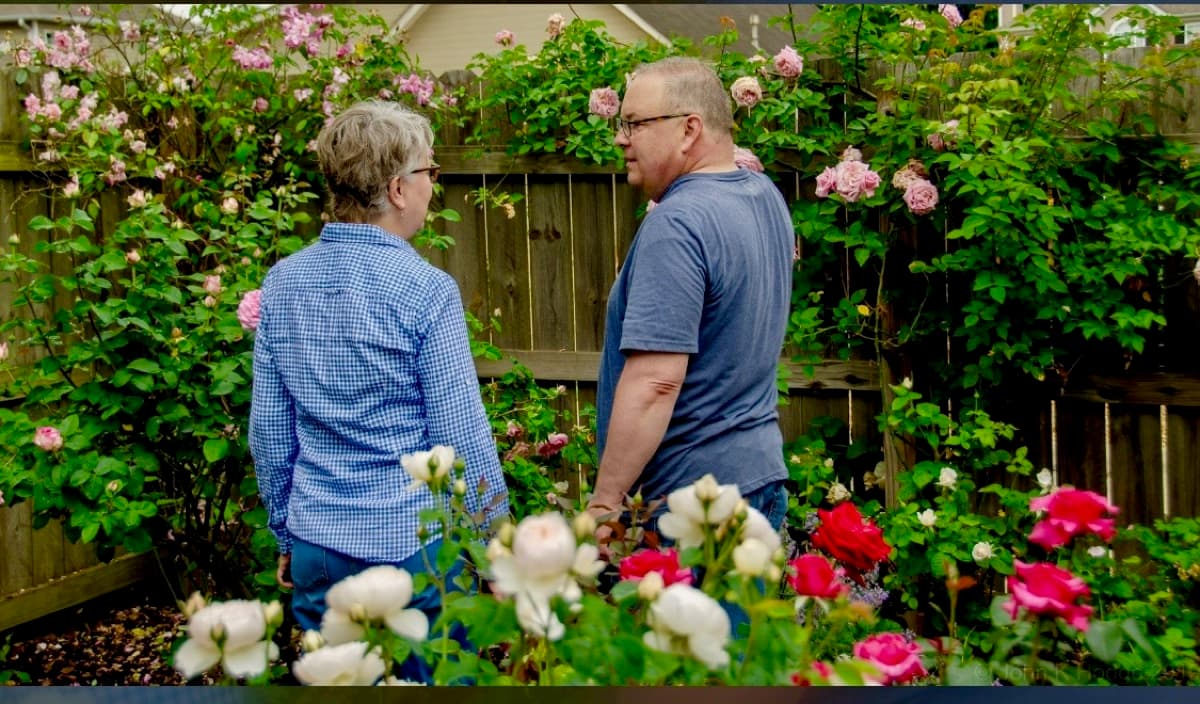 Chris VanCleave and his wife talking among climbing roses in their garden