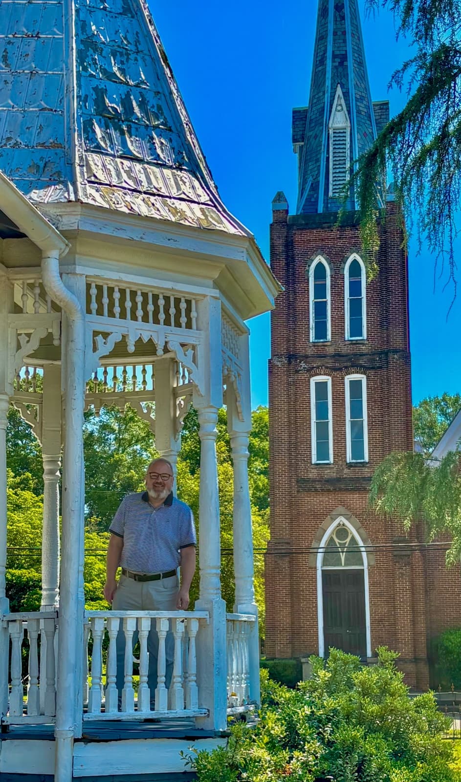 Chris VanCleave standing in a historic gazebo in Marion, Alabama, with a church steeple in the background
