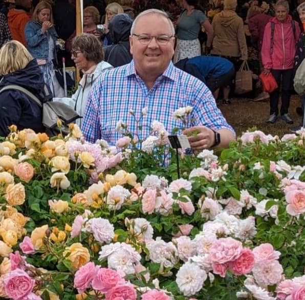 Chris VanCleave smiling behind a display of pink and apricot roses at a rose show