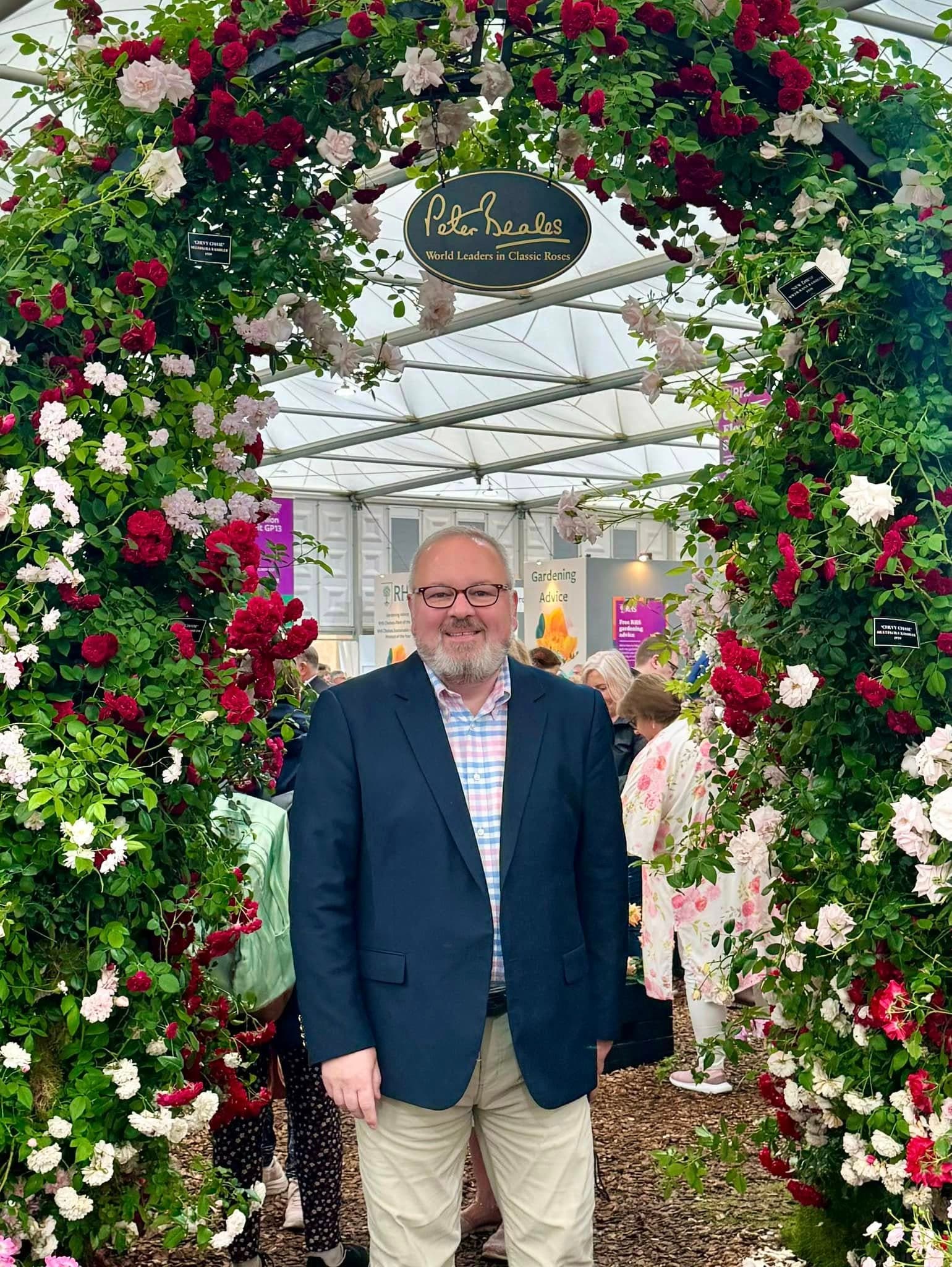 Chris VanCleave smiling beneath a rose covered arch at the Peter Beales rose display
