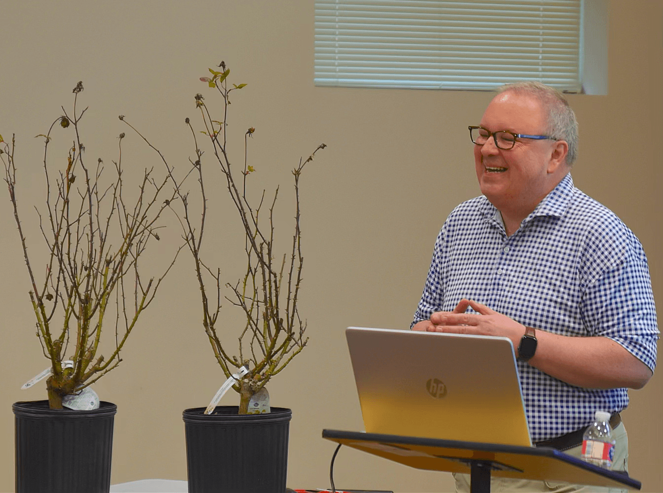 Chris VanCleave laughing while speaking at a podium next to two bare root rose displays