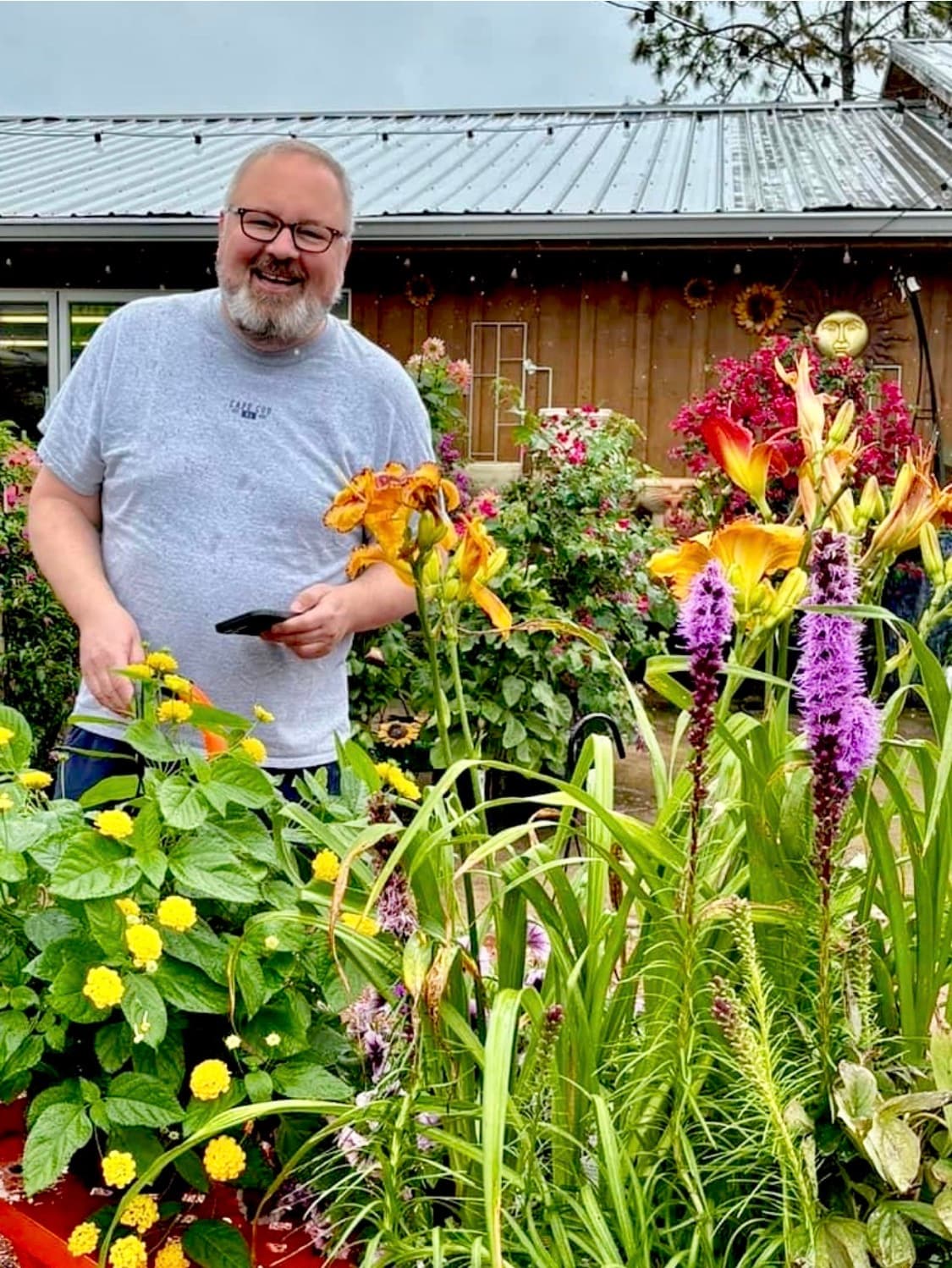 Chris VanCleave smiling among summer blooms and lilies in a garden center display