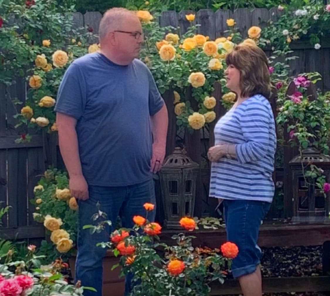 Chris VanCleave talking with his wife among yellow and orange roses in their backyard garden